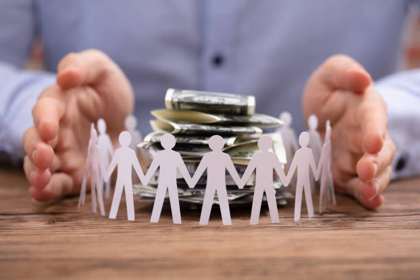 Person's Hand Protecting Stacked Banknotes Surrounded By Human Figures